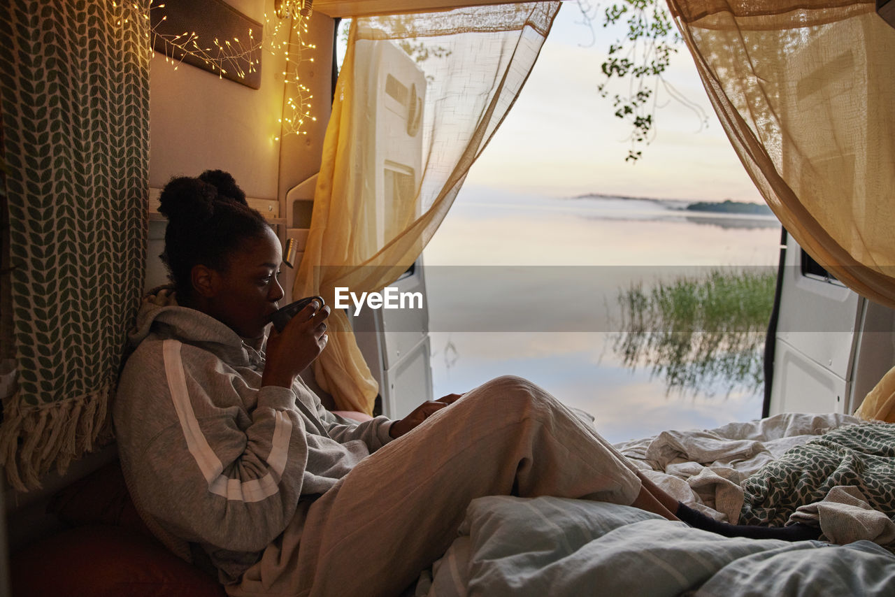 Woman sitting in bed in camper van and drinking tea