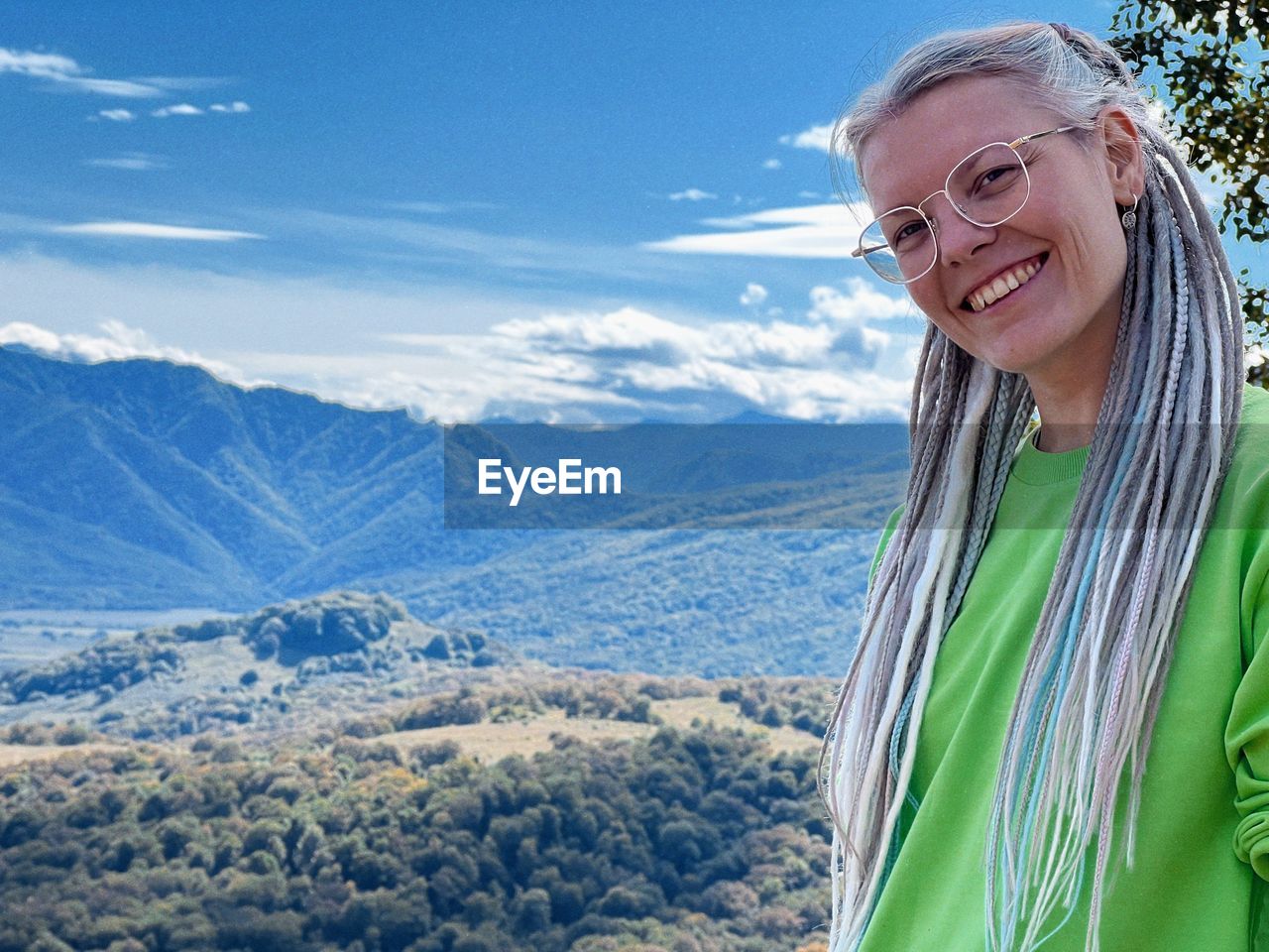 mountain, smiling, adult, one person, portrait, happiness, mountain range, leisure activity, nature, scenics - nature, environment, emotion, landscape, women, senior adult, beauty in nature, mature adult, vacation, looking at camera, sky, day, glasses, lifestyles, seniors, holiday, cheerful, trip, travel, winter, standing, smile, teeth, person, clothing, outdoors, cold temperature, waist up, sunlight, tranquil scene, female, travel destinations, tranquility, snow, eyeglasses, enjoyment, non-urban scene, retirement, gray hair, adventure, land, hiking, human face, positive emotion, activity, looking, cloud, summit, rural scene, casual clothing, headshot, blue, blond hair, relaxation