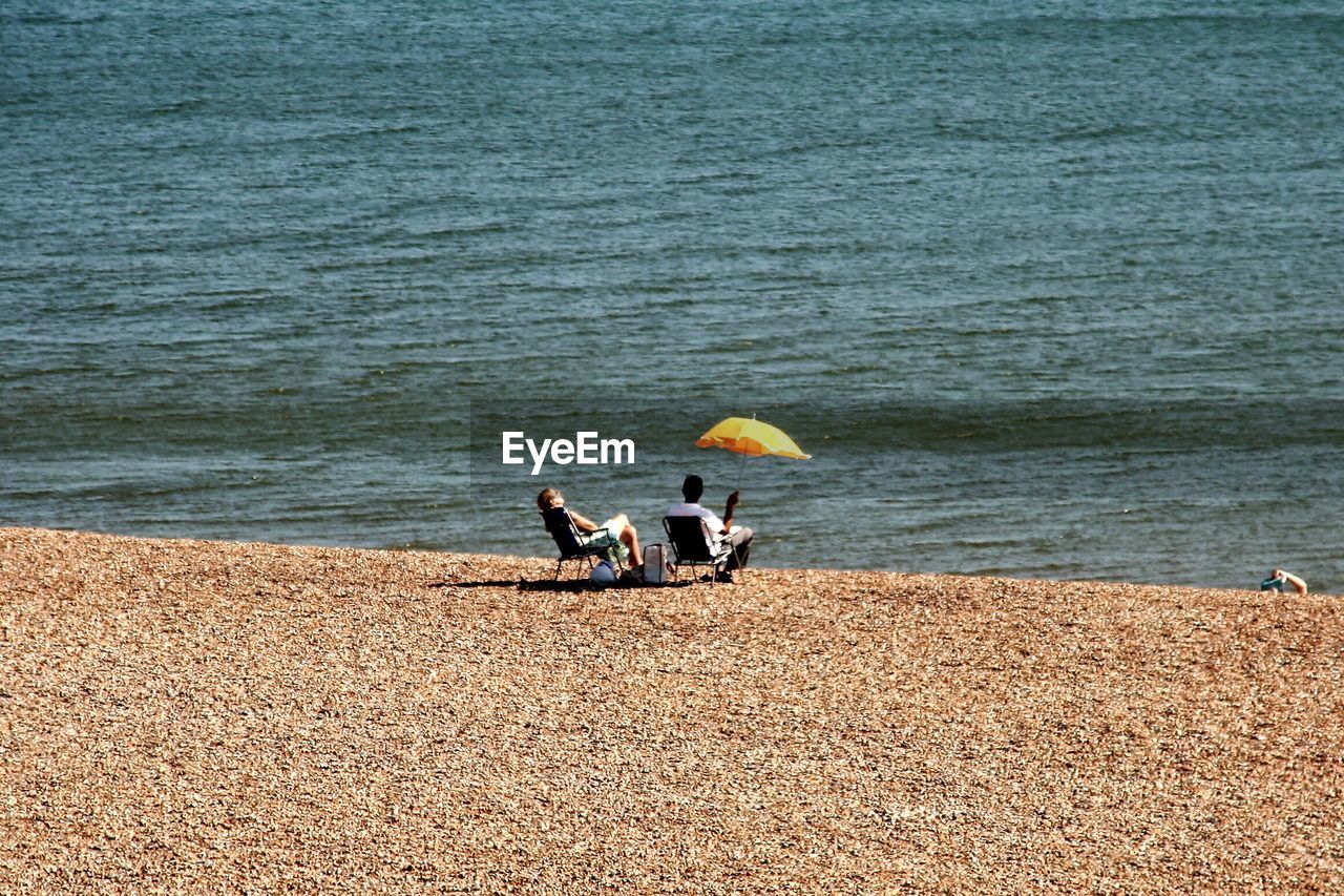 Rear view of couple relaxing on shore at beach