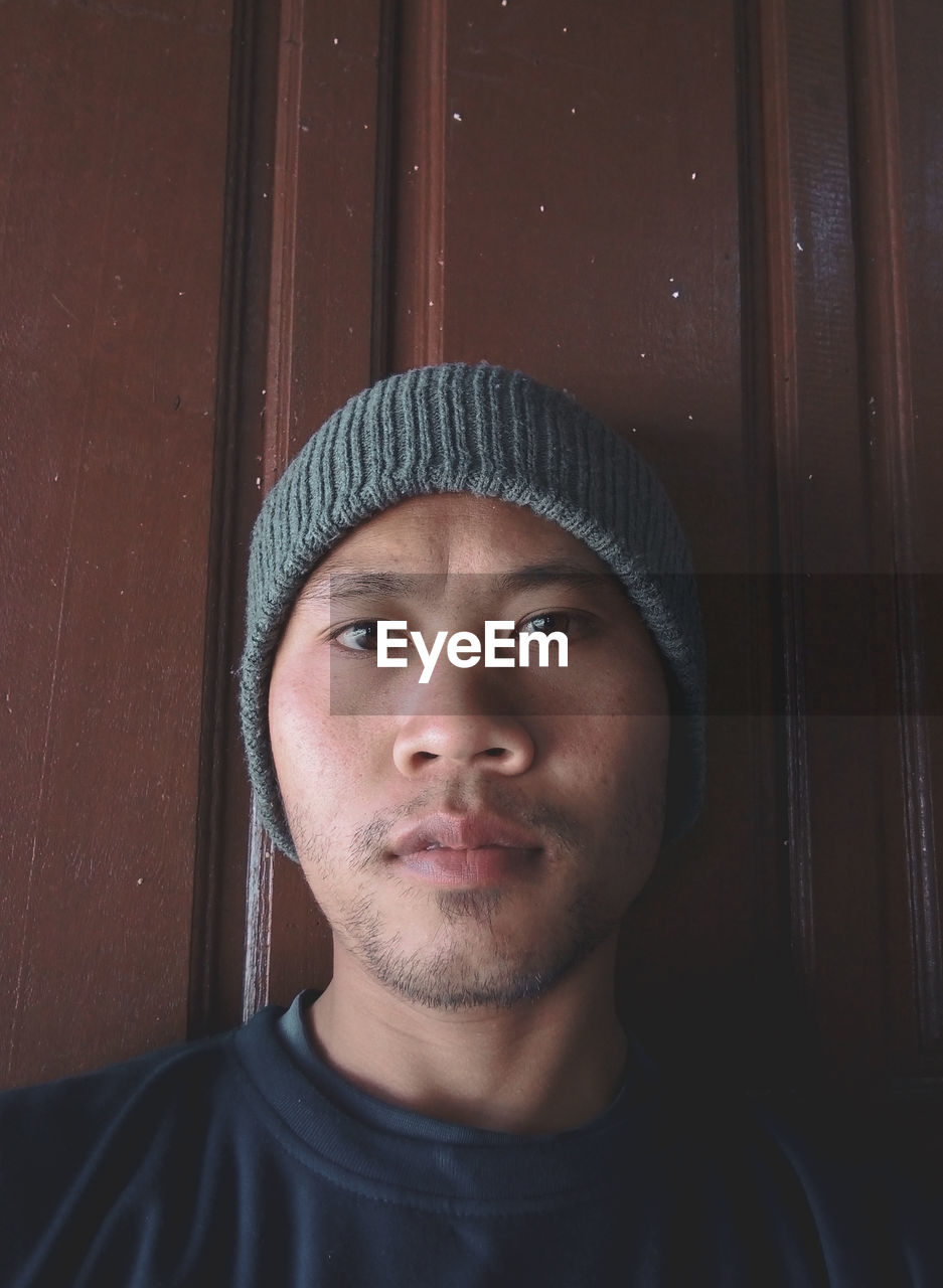 CLOSE-UP PORTRAIT OF YOUNG MAN AGAINST DOOR