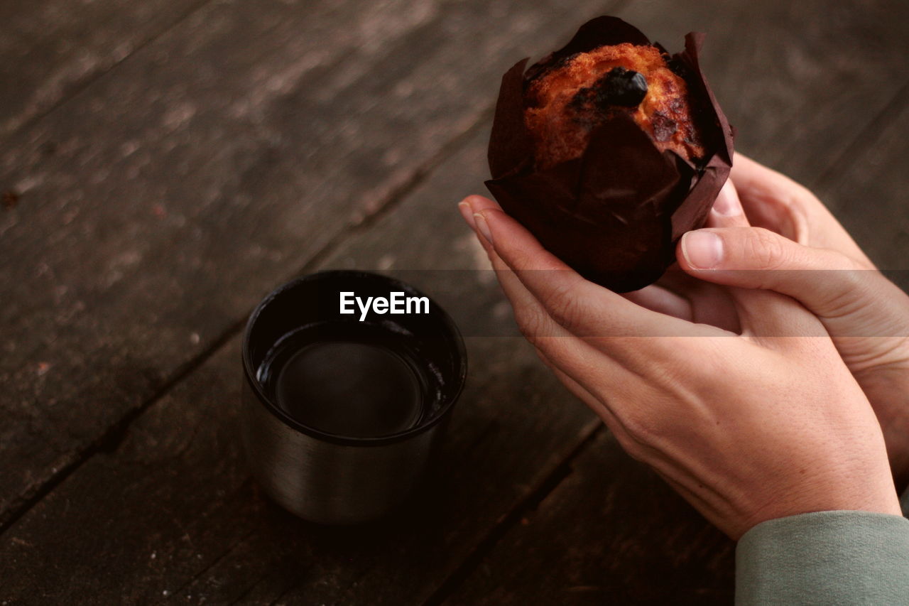 Muffin in female hands near a thermos on a wooden background outdoors