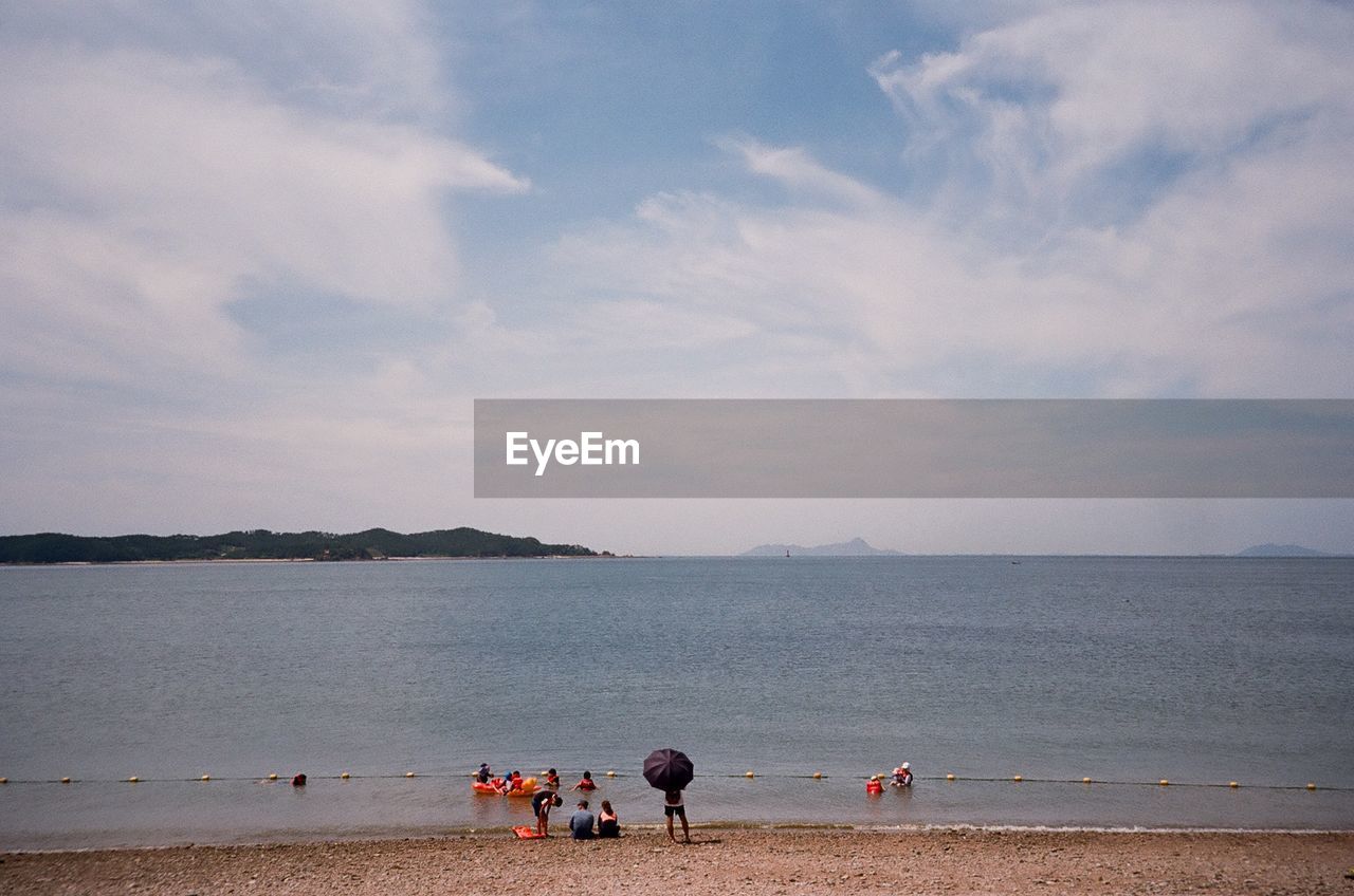 PEOPLE ON BEACH AGAINST SEA