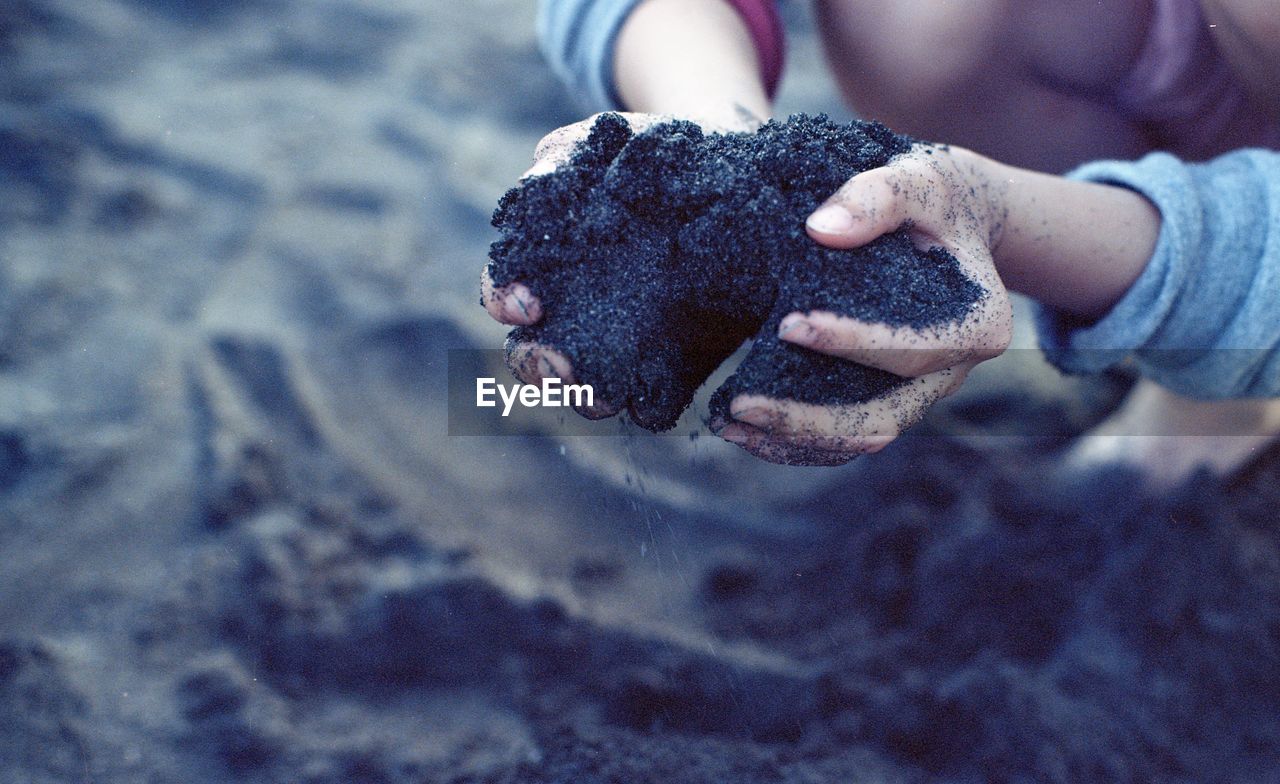 Cropped image of kid hands holding black sand at beach