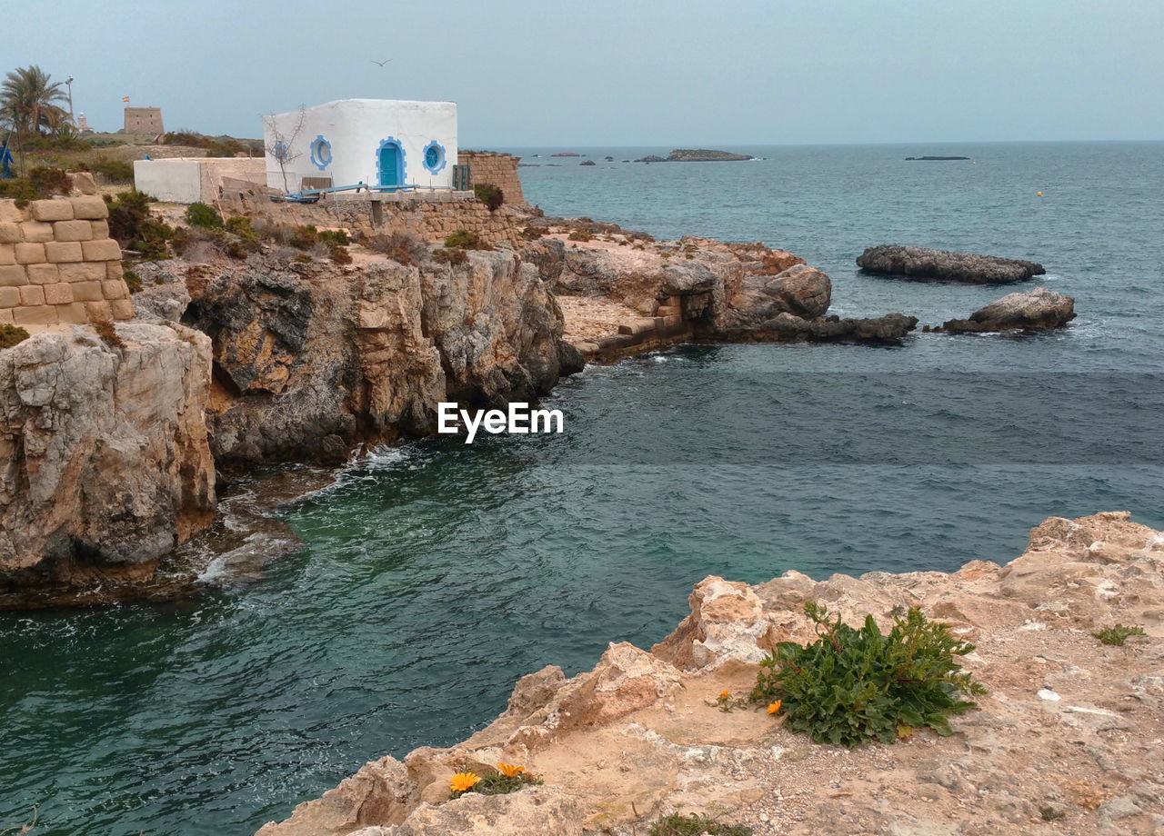 Scenic view of sea and small house on rocks against clear sky