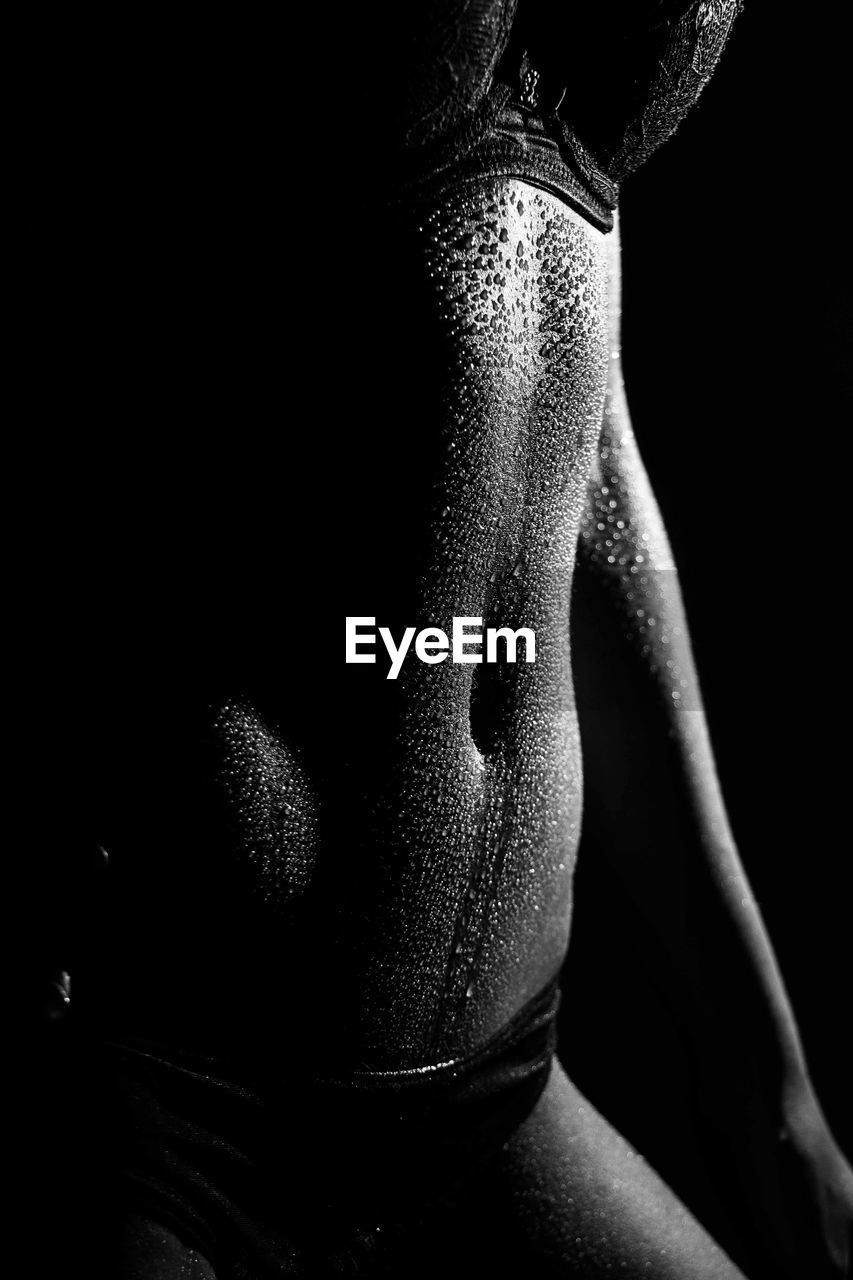 Midsection of woman sweating against black background