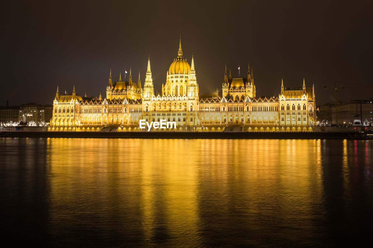 Illuminated building by river at night