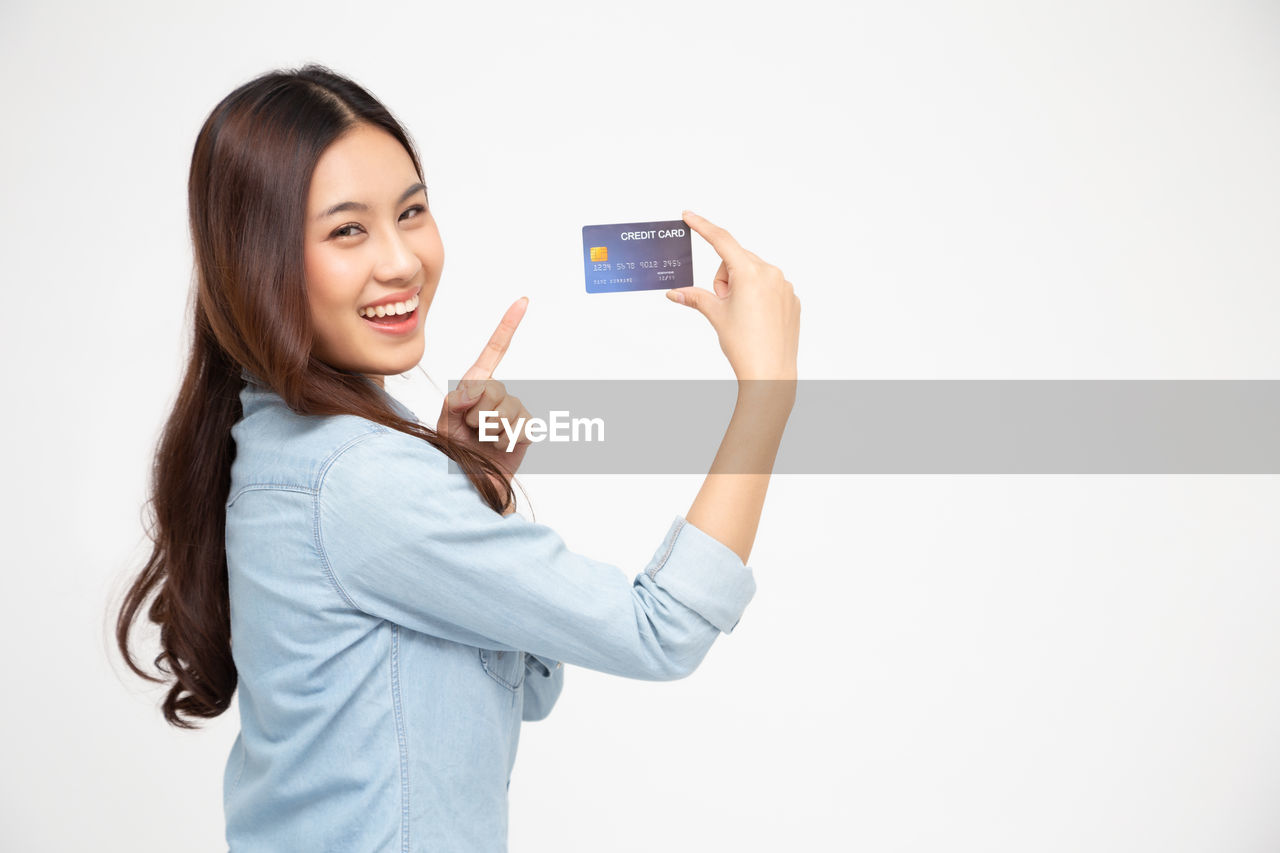 PORTRAIT OF SMILING YOUNG WOMAN USING SMART PHONE