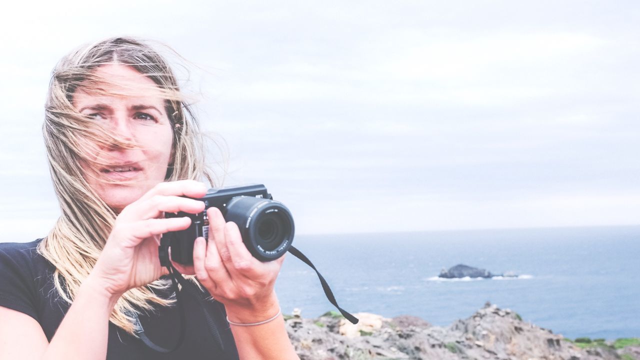 Close-up of woman with camera against sky