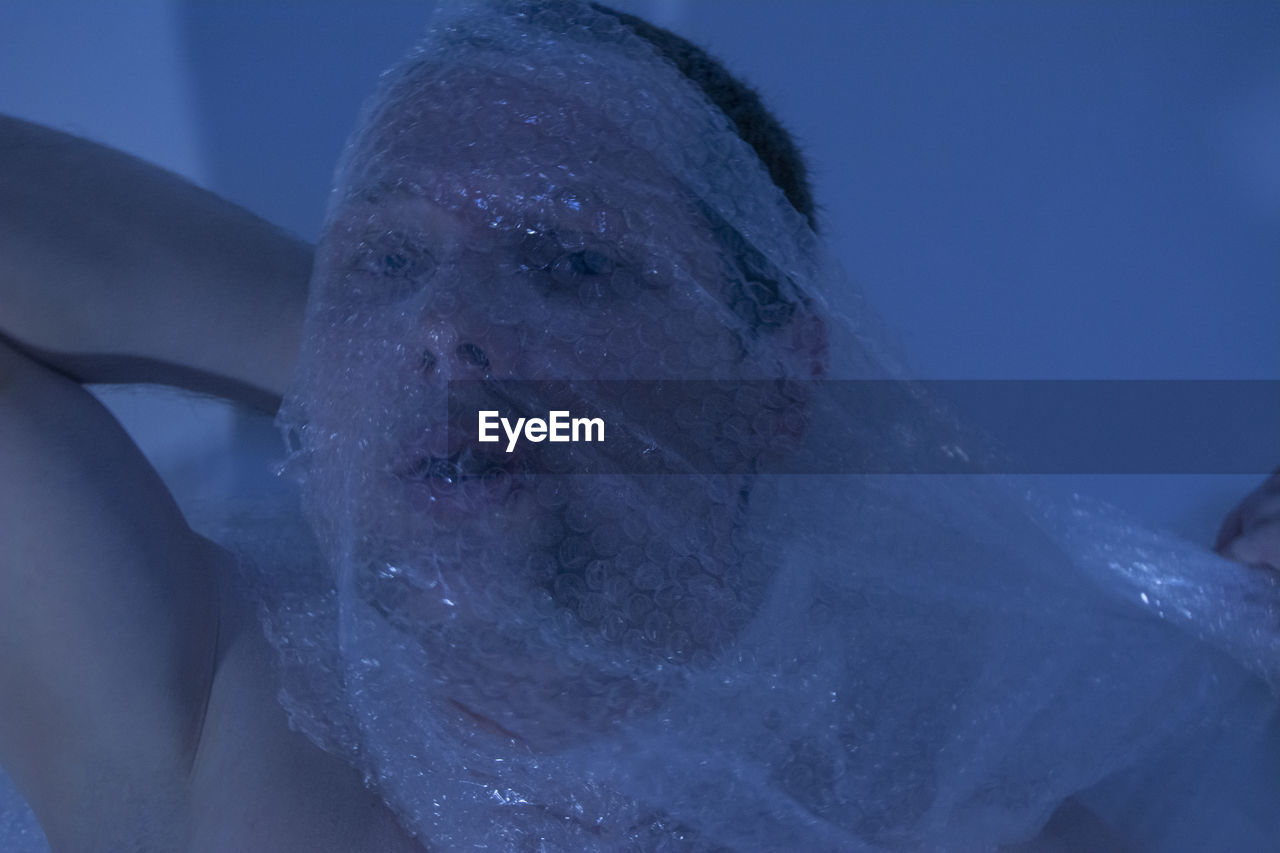 Close-up portrait of man covering face with bubble wrap at home