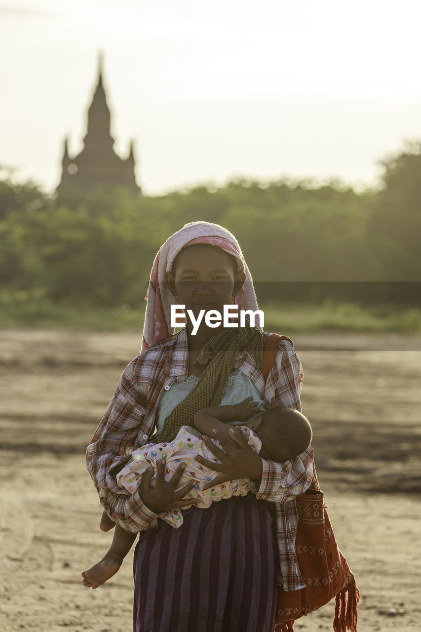 MIDSECTION OF WOMAN STANDING BY CROSS ON LAND