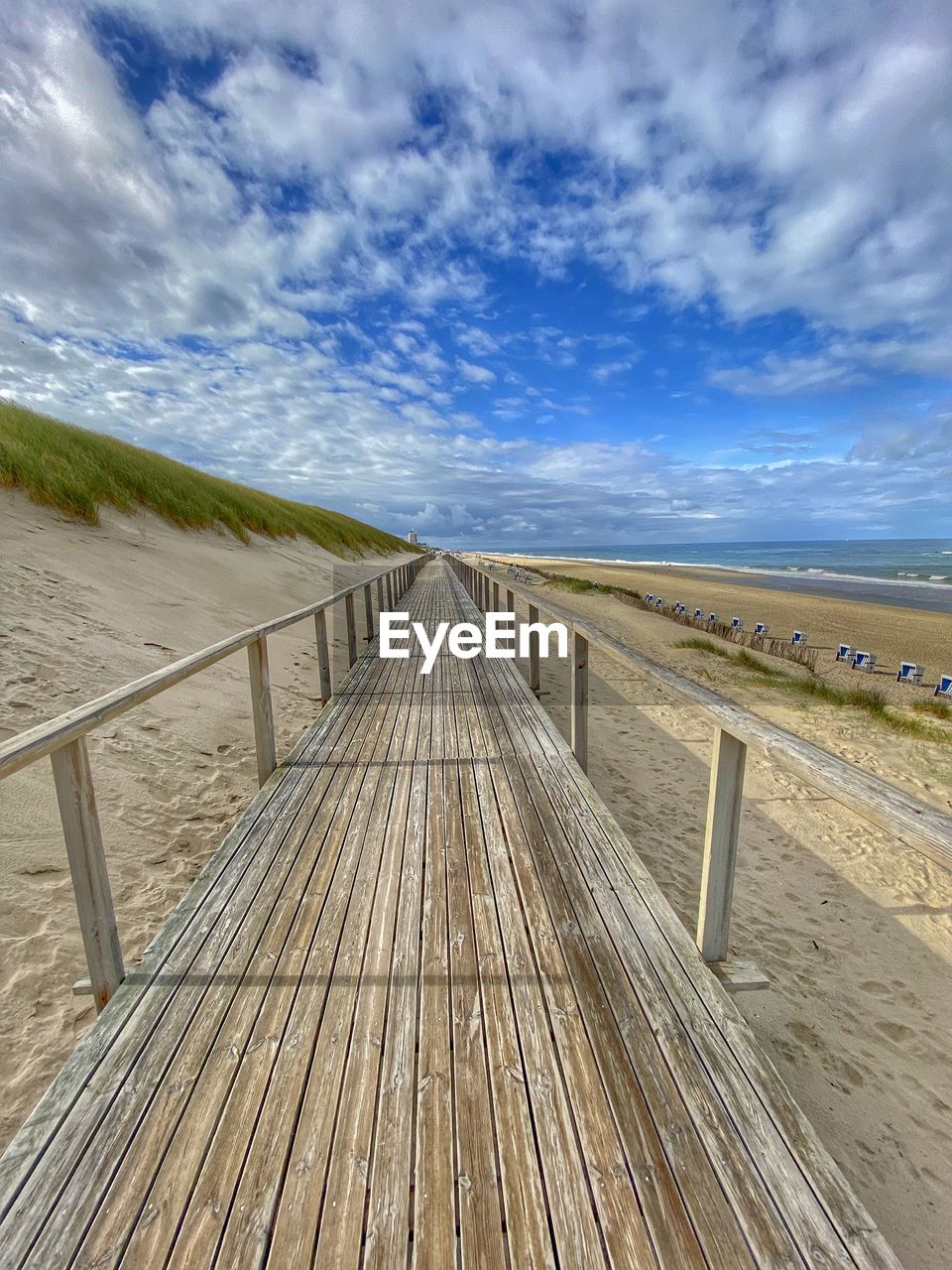 Empty boardwalk leading towards beach against sky