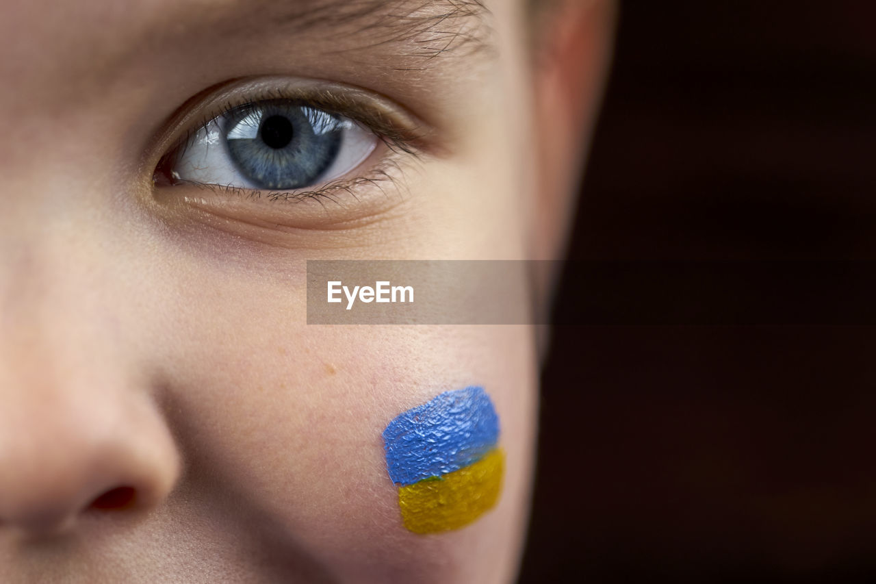 Child's eye and ukrainian flag is drawn on his cheek