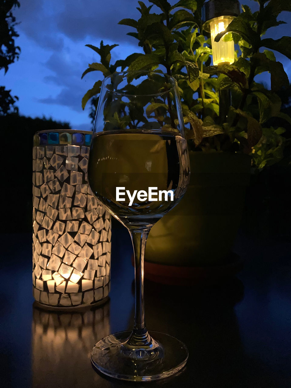 CLOSE-UP OF WINE GLASS ON TABLE AGAINST ILLUMINATED LAMP