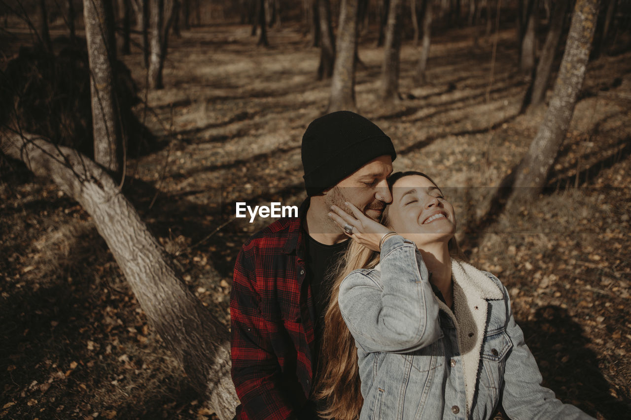 Couple sitting on tree in forest during sunny day