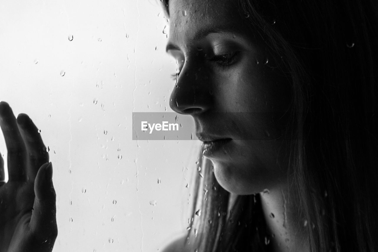 Close-up of young woman seen through wet glass