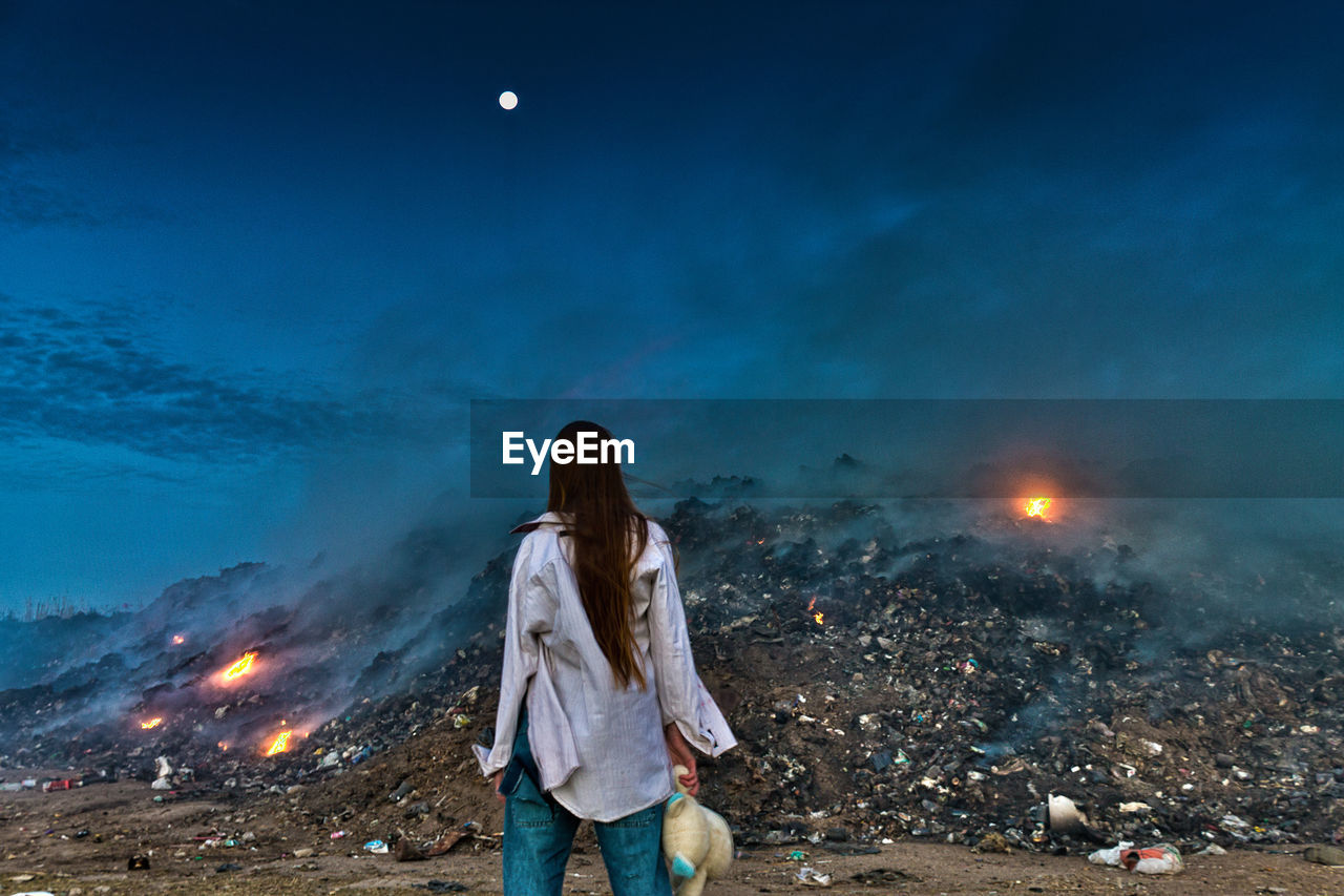 Rear view of woman standing against junkyard at night