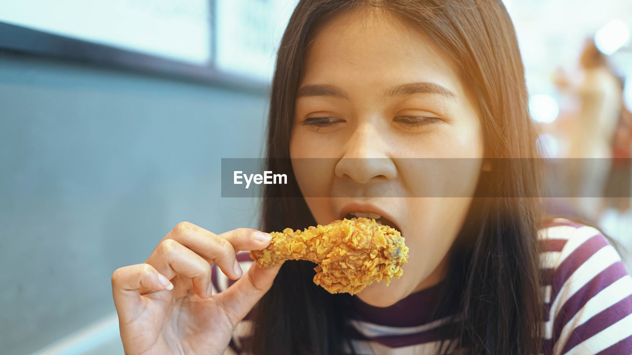 Close-up of young woman eating fried chicken sitting at restaurant