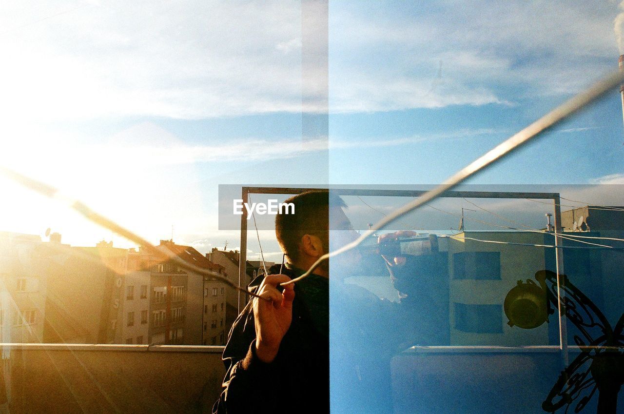 Man skateboarding on glass window against sky