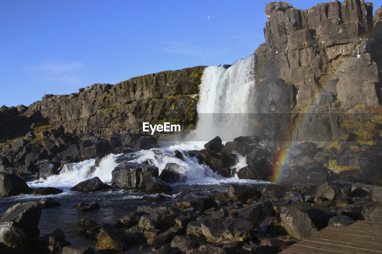 waterfall, water, rock, cliff, scenics - nature, environment, nature, terrain, beauty in nature, sky, motion, land, travel destinations, water feature, mountain, landscape, body of water, coast, travel, geology, blue, sea, rock formation, formation, outdoors, no people, tourism, long exposure, splashing, wilderness, non-urban scene, clear sky, flowing