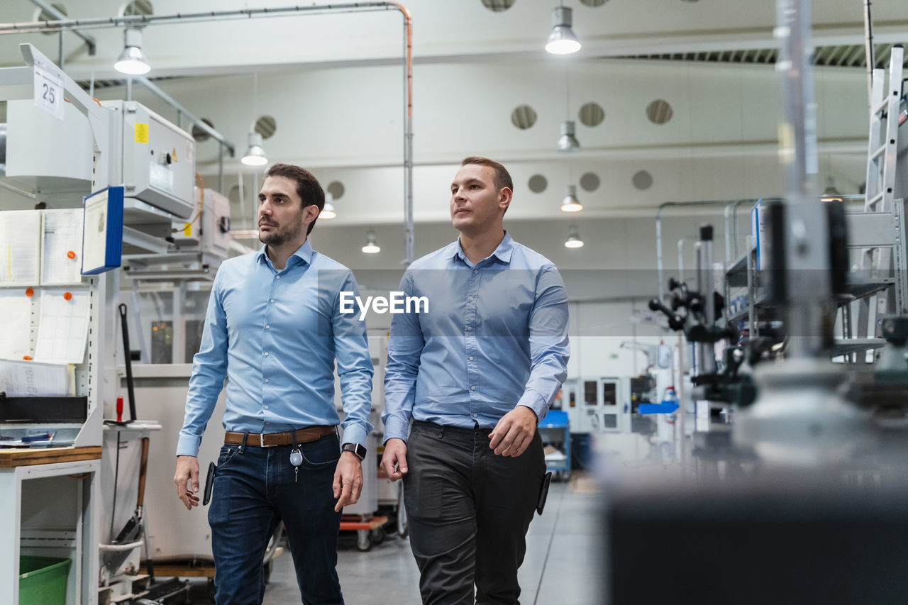 Male inspectors examining machine while walking at factory