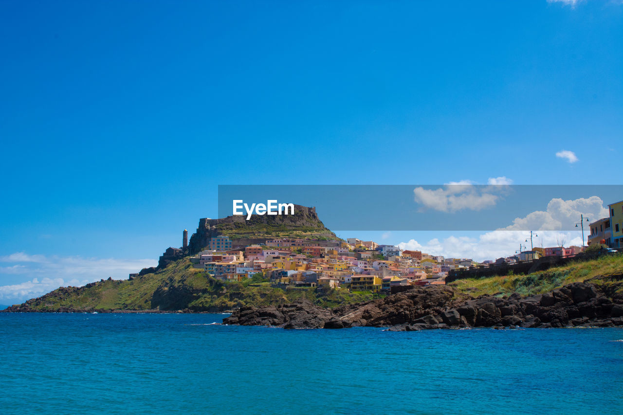 Buildings on mountain by sea against blue sky at castelsardo