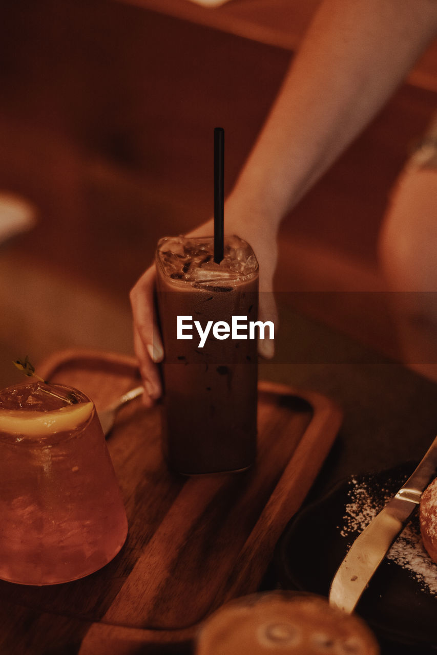 CLOSE-UP OF HAND HOLDING DRINK WITH ICE TEA