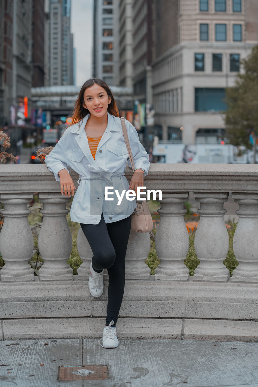 portrait of smiling young woman standing against built structures