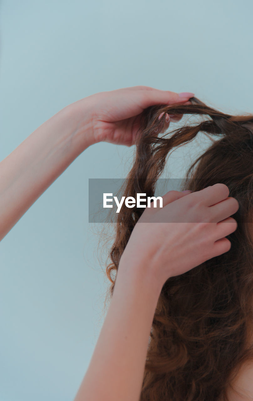 Cropped hands doing hairstyle for woman against wall