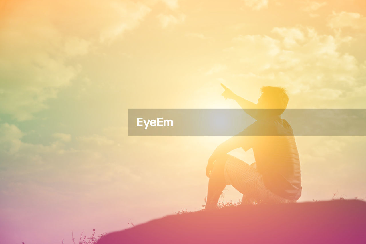 Side view of silhouette man sitting on land against sky during sunset