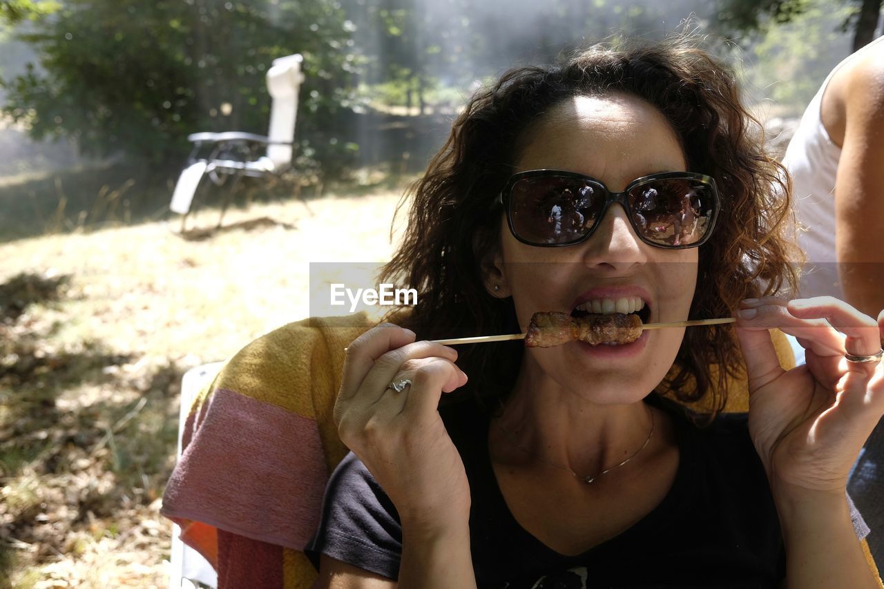 Woman eating arrosticini on field during sunny day