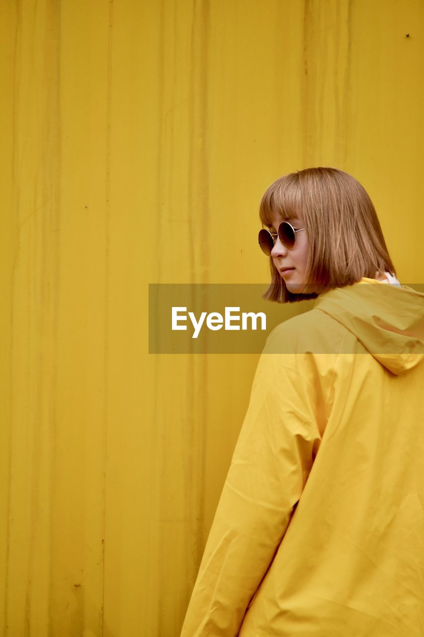 Young woman wearing sunglasses standing against yellow corrugated iron