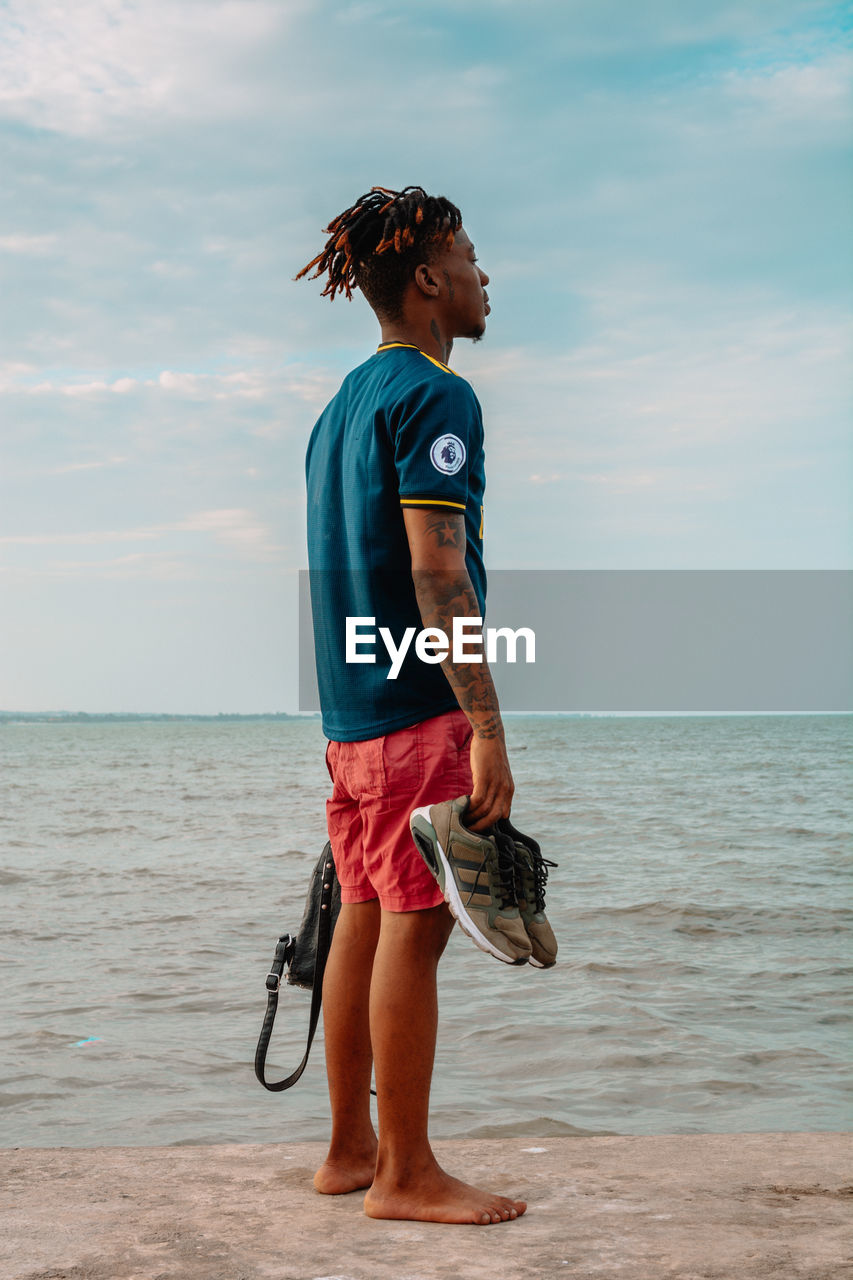 FULL LENGTH OF MAN STANDING ON BEACH AGAINST SEA