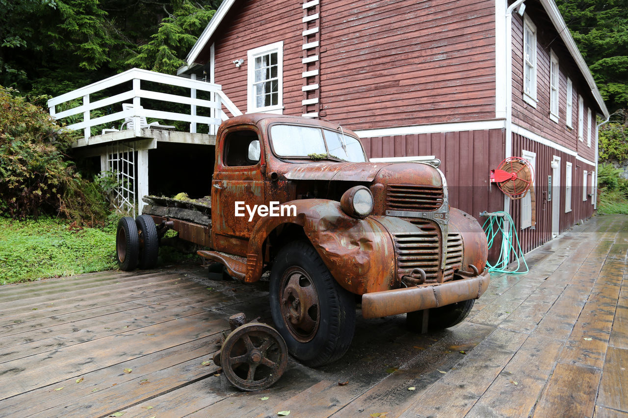 VIEW OF ABANDONED CAR ON ROAD BY OLD BUILDINGS