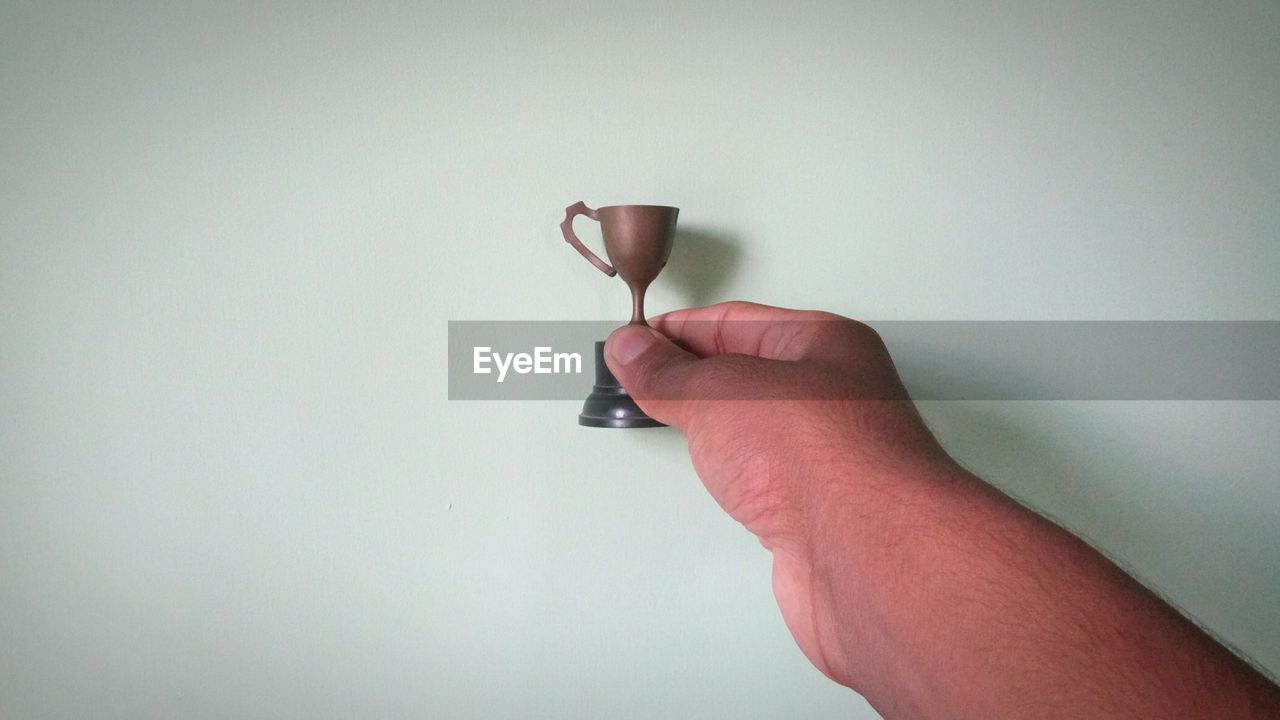 Close-up of hand holding small trophy against wall