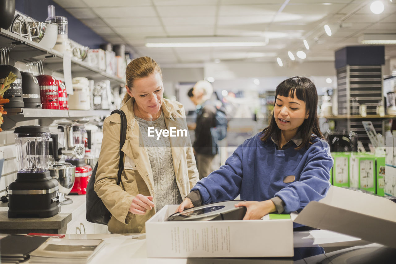 Saleswoman unboxing appliance for customer in store