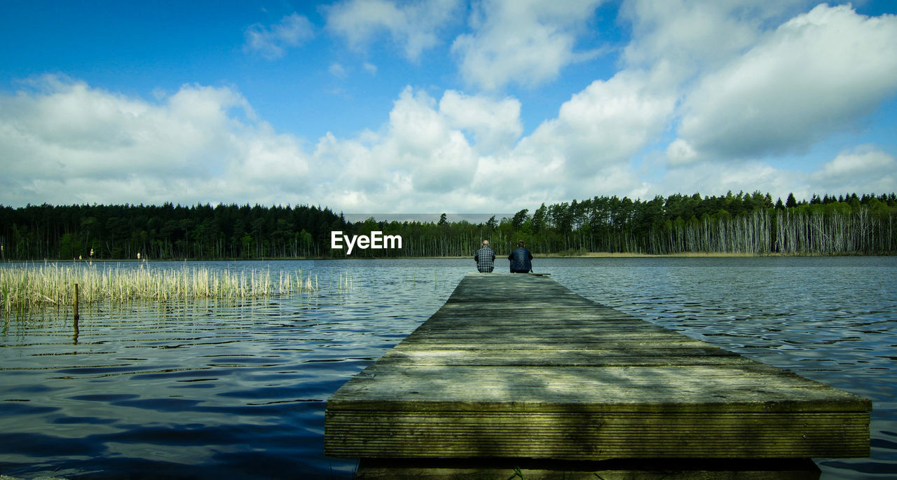 Rear view of people on pier over lake against sky