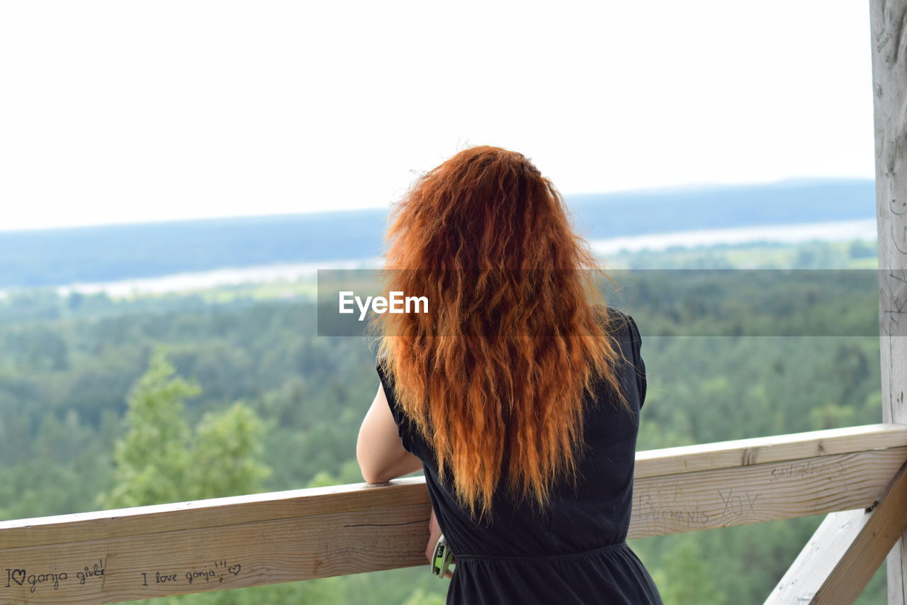 Rear view of woman leaning on railing against green landscape