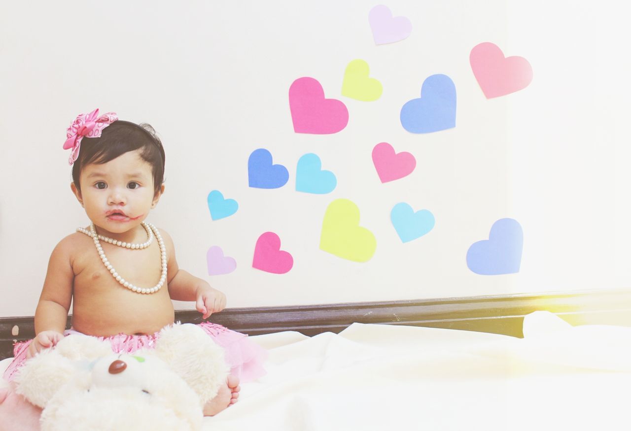 Shirtless baby girl looking away while sitting on bed at home