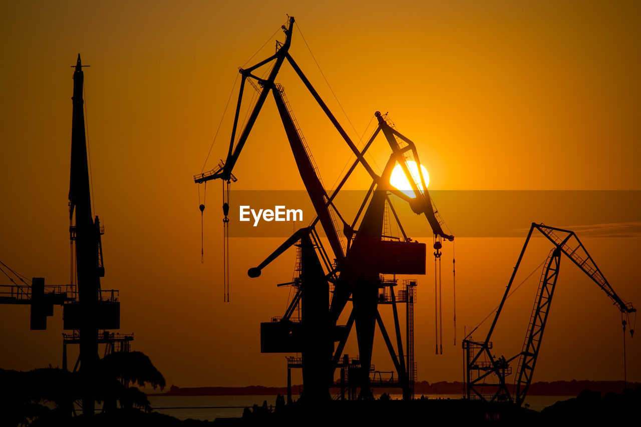 Silhouette cranes against sky at sunset at port of pula, croatia