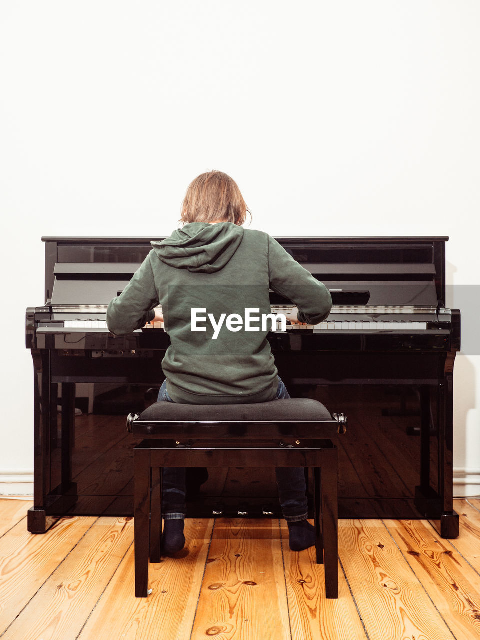 Rear view of boy playing piano at home