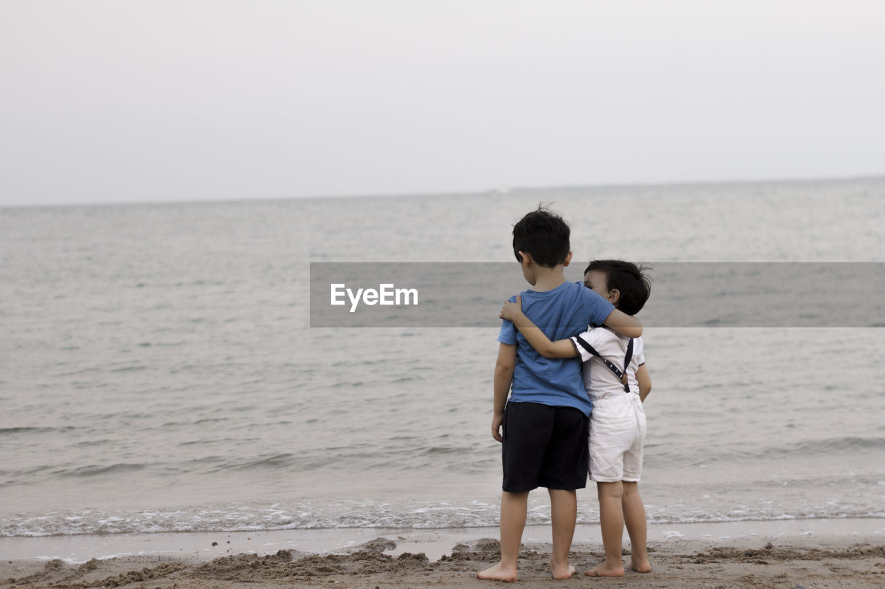 Two boys looking the sea, while hugging each other