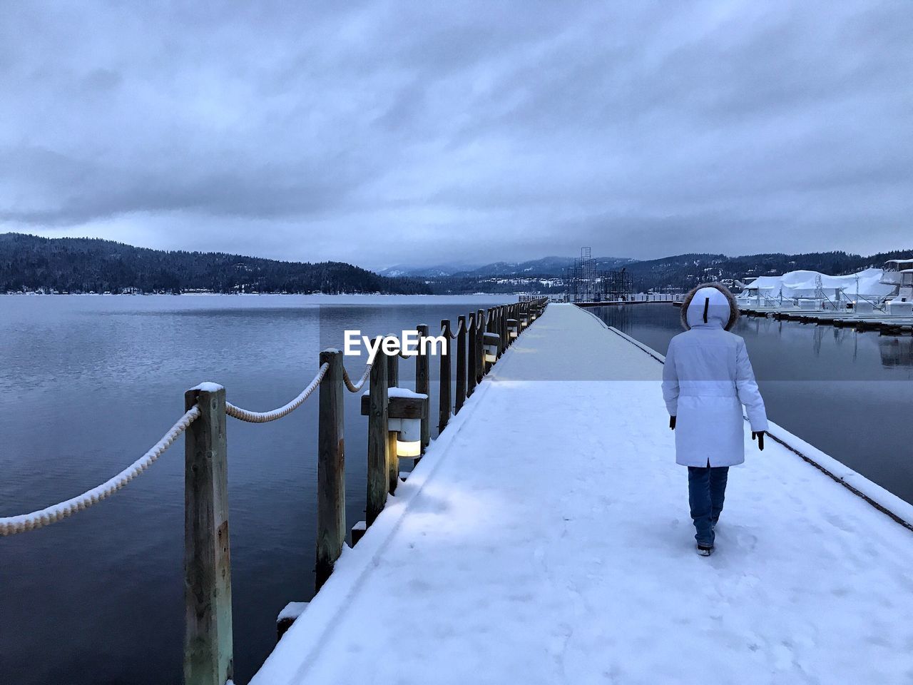 Rear view of woman walking on snow covered pier over frozen lake during winter