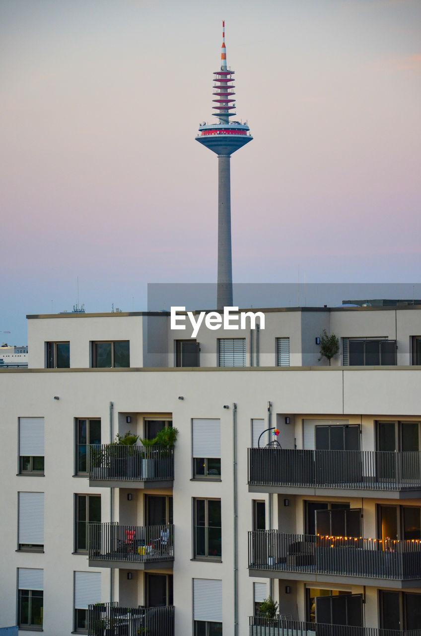 Low angle view of communications tower behind building against sky