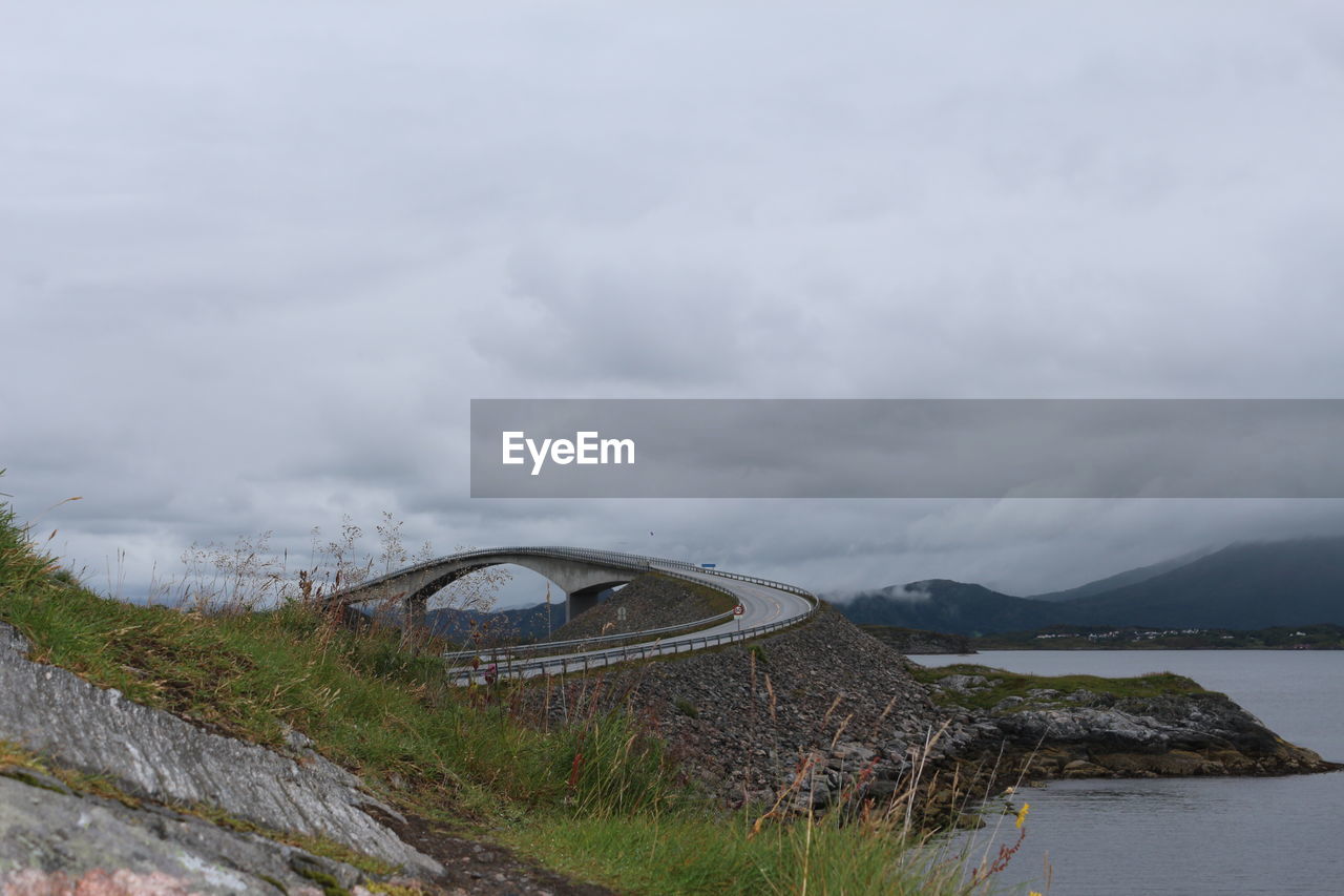 Bridge by mountain against cloudy sky