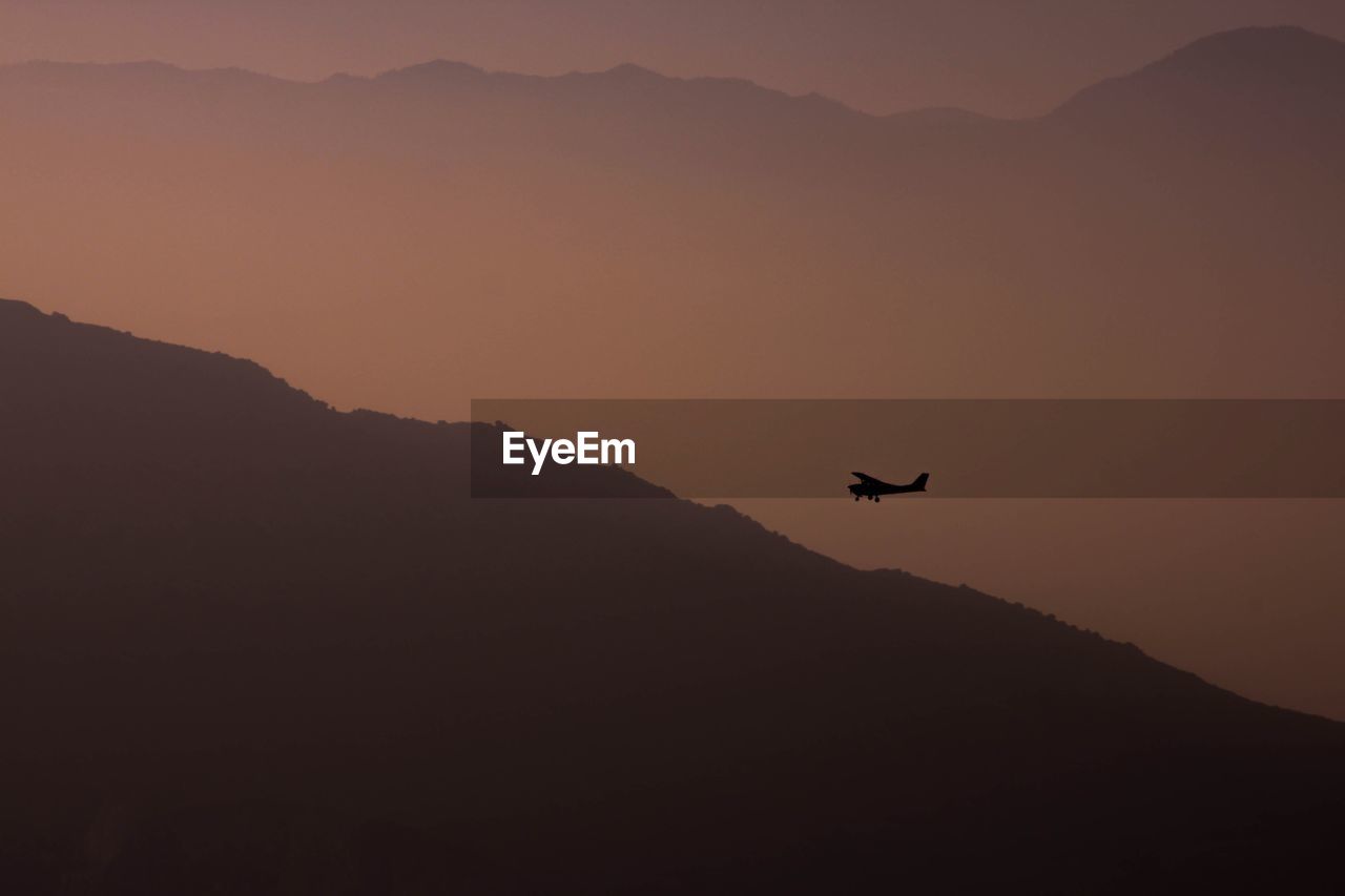 Silhouette of plane flying over mountain against sky during sunset