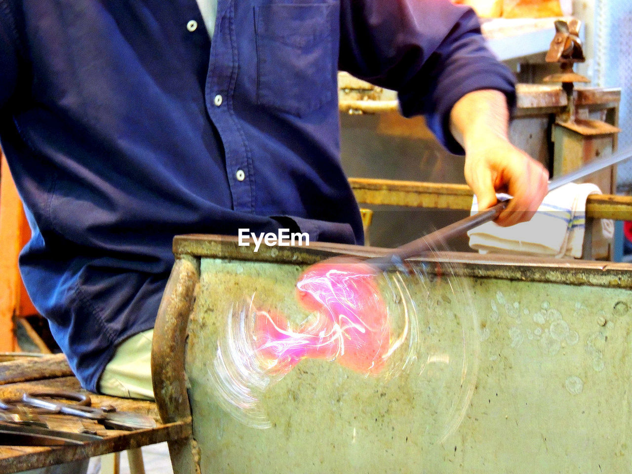 Midsection of worker spinning glass blower at factory