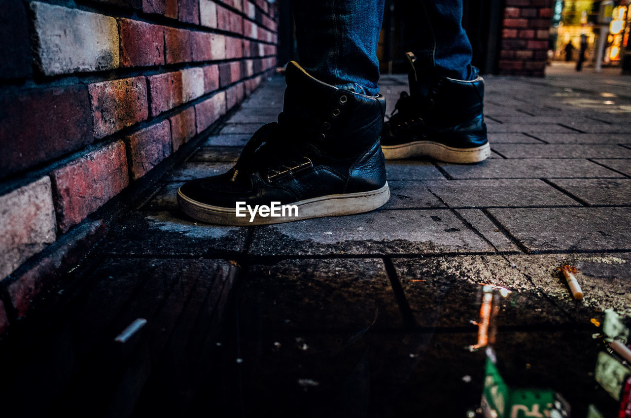 Low section of man standing on sidewalk by brick wall