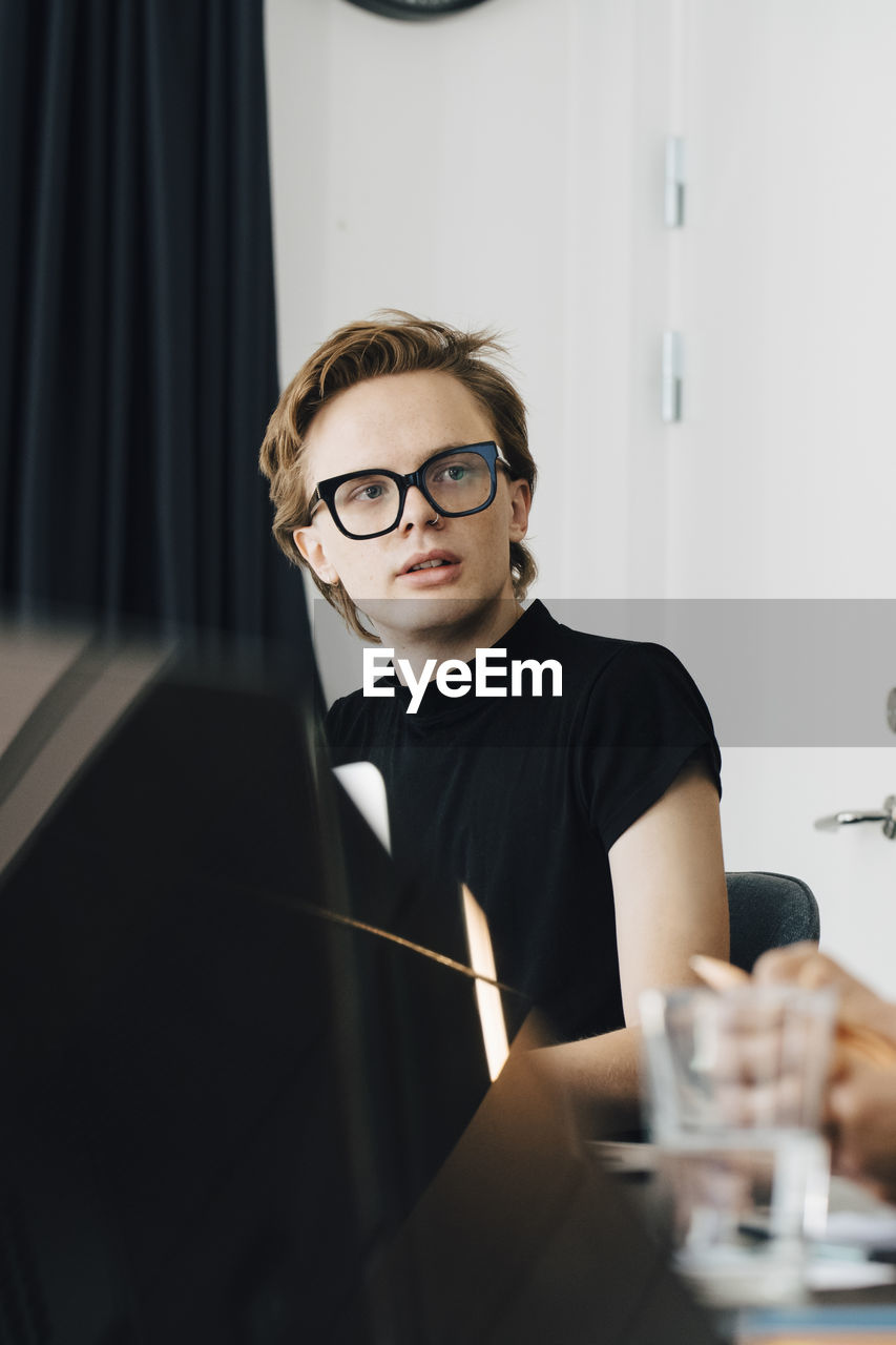 Young genderblend professional looking away while sitting in board room during meeting