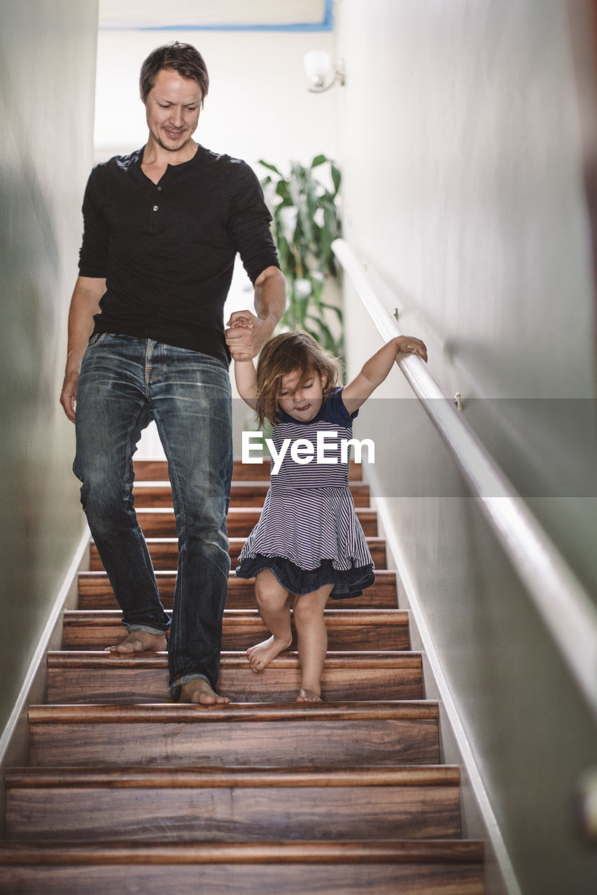 Smiling father holding hands with daughter while climbing steps at home