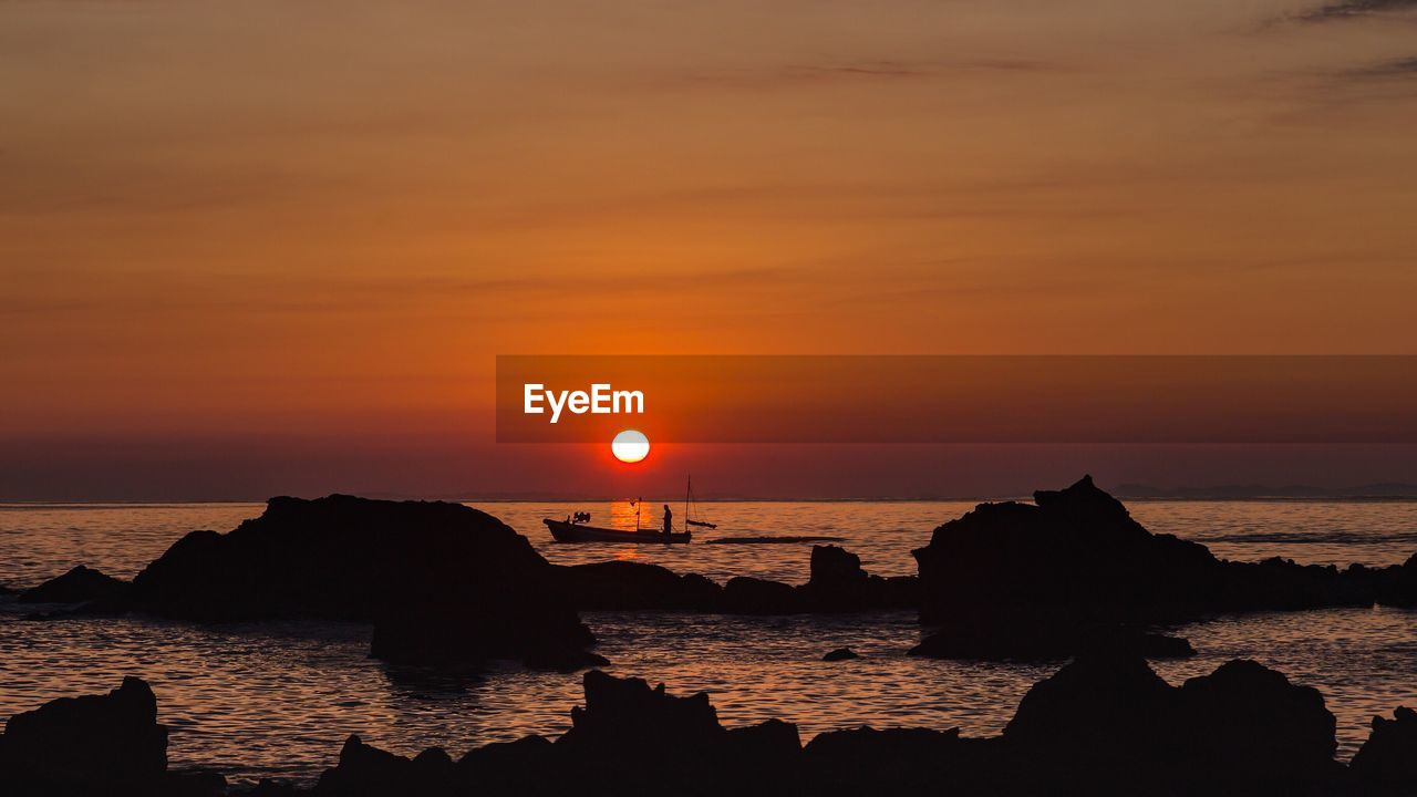 Silhouette boat on sea against orange sky